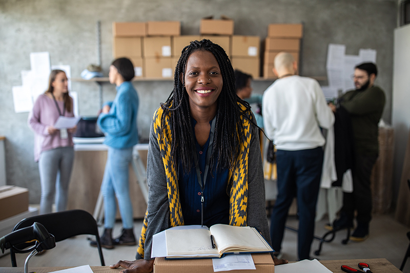 Young African female entrepreneur with long braided working alongside her coworkers in e-commerce office